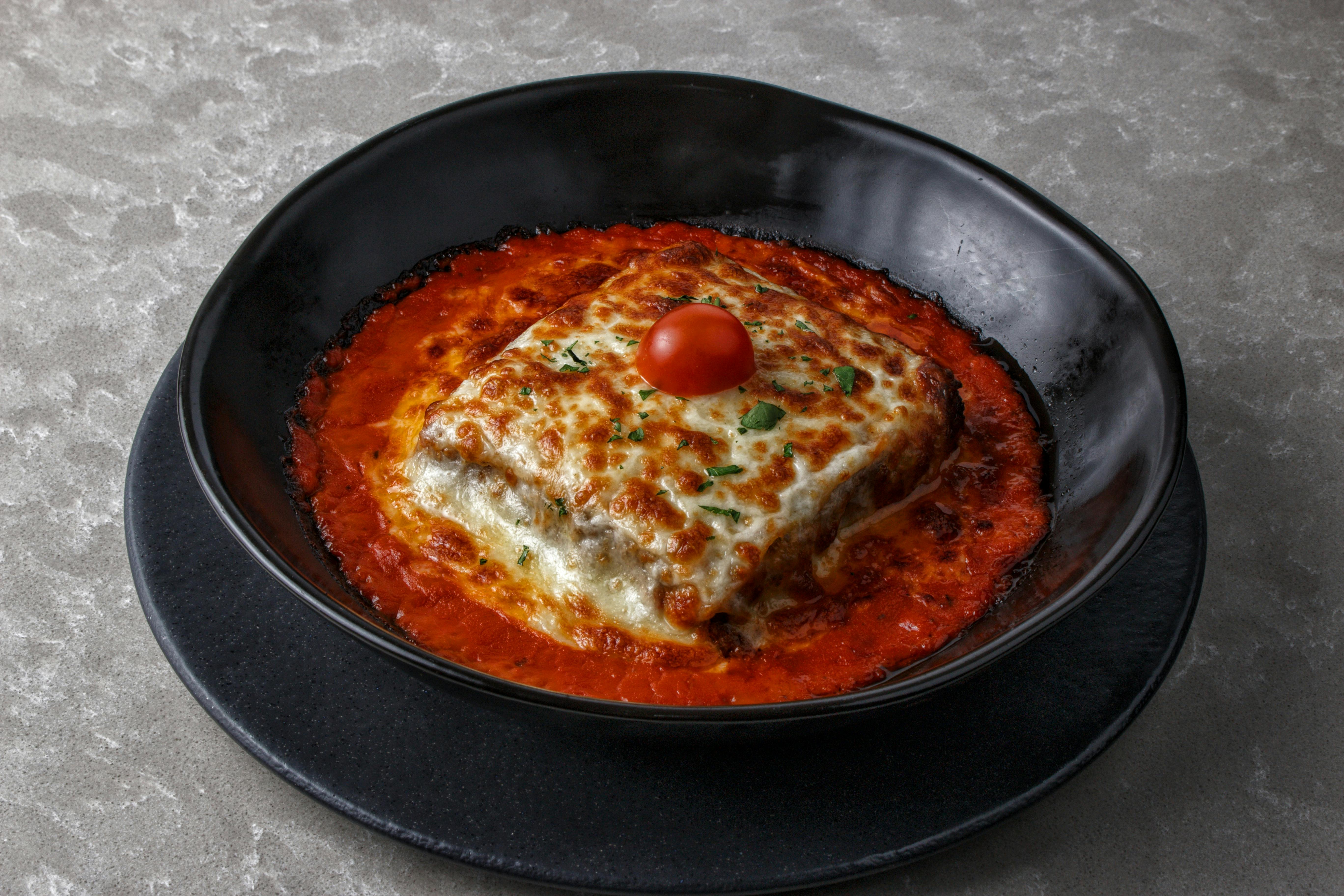 A lasagna slice with tomato sauce served in a black round dish